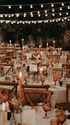 tables and chairs are set up for an event with lit candles in the middle, surrounded by greenery