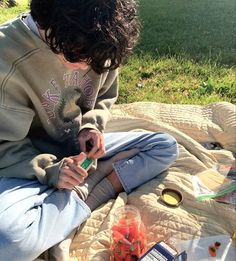 a person sitting on a blanket with food and drinks in front of them at the park