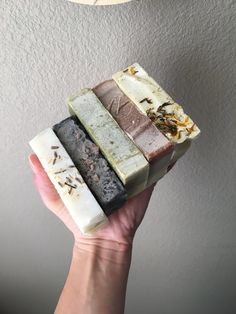 a hand holding four different soap bars in front of a white ceiling light and a gray wall