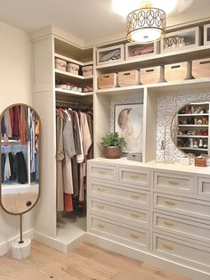 an organized closet with white drawers and large mirror on the wall, along with clothes hanging in bins