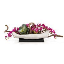 a white boat filled with purple flowers on top of a wooden table next to a planter