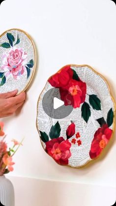 two plates with flowers painted on them are being held up by someone's hand