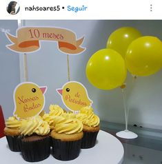 two cupcakes with yellow frosting are on a plate next to some balloons