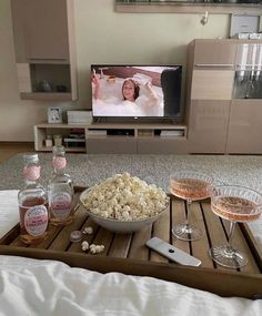 a tray with popcorn, wine glasses and bottles on it in front of a flat screen tv