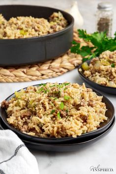 two black plates filled with rice and vegetables next to a basket full of parsley