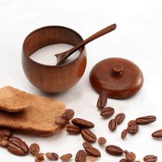 a bowl of milk and some nuts on a white surface with a wooden spoon next to it