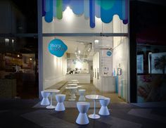 several white tables and stools are in front of a storefront window at night