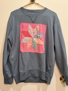 a blue sweatshirt with an embroidered star on the front hanging from a hanger against a wall