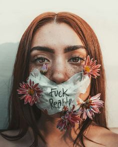 a woman with flowers on her face and the words f k reality taped to her mouth