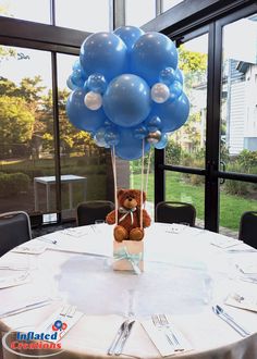 a teddy bear sitting on top of a table with blue balloons in the shape of a heart