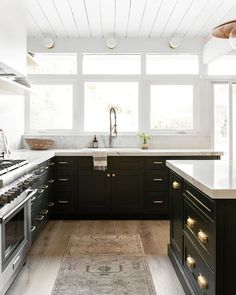 a kitchen with black cabinets and white counter tops, an oven and sink are in front of the window