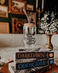 three books stacked on top of each other in front of a vase with a straw sticking out of it