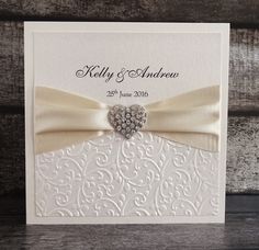 a white wedding card with a heart on the front and bow at the back, sitting on a wooden surface