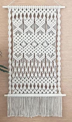 white crocheted wall hanging next to a plant on a wooden table with flowers