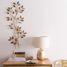 a lamp on top of a wooden dresser next to a wall mounted metal tree branch