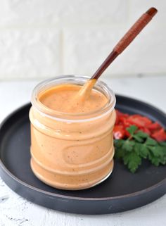 a glass jar filled with sauce sitting on top of a black plate next to tomatoes and cilantro