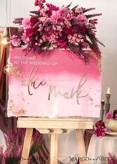 a pink and gold wedding welcome sign with flowers on the top is sitting on a easel