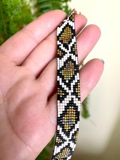 a hand holding a beaded bracelet in front of a plant