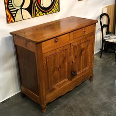 a wooden cabinet sitting in front of a wall with paintings on the wall behind it