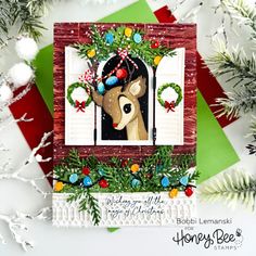 a handmade christmas card with a deer in the window and wreaths around it