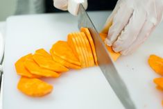 a person in white gloves cutting carrots with a knife