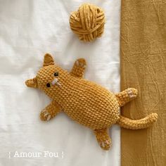 a crocheted cat and ball of yarn sitting on a white sheet next to each other