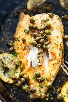 a piece of fish with lemons and capers on the side in a skillet