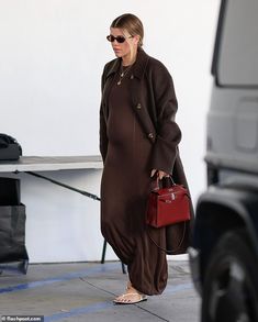 the woman is walking down the sidewalk carrying her handbag and wearing brown dress with matching heels