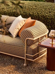 a couch sitting on top of a gravel covered ground next to a table and bushes