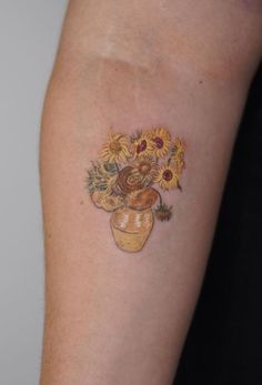 a woman's arm with sunflowers in a vase tattoo on the left upper arm