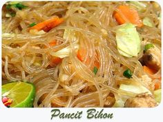 a plate of food with noodles, carrots and meat on it next to a lime slice