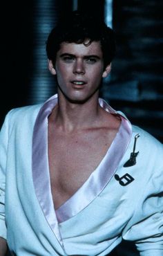 a male model in a white suit and tie with his shirt draped over his shoulders