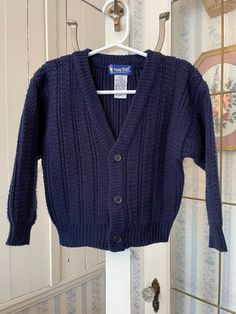 This adorable Young Street cardigan from The Bay is made of soft, 100 per cent acrylic in a chunky, dark navy blue knit. It has the original buttons in the front. Marked size small/4. The measurements, taken with the sweater lying flat, are: shoulder to shoulder, 12 1/2 inches; armpit to armpit, 13 1/2 inches; sleeves, 13 inches; length, 14 inches; bottom edge, 10 inches (with stretchy ribbing). The sweater overall has a bit of stretch. In very good condition. Navy Cardigan With Button Closure For Winter, Navy Button-up Sweater For Fall, Navy Button Sweater For Fall, Classic Navy Knitted Sweater, Blue Knit Cardigan, Kids Jumpers, Navy Cardigan, Navy Blue Sweater, Knit Cardigan Sweater