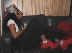 a woman sitting on top of a black couch next to a red backpack and wearing a hat