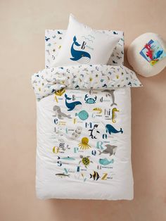 a white bed with blue and yellow sea animals on it, next to a round pillow