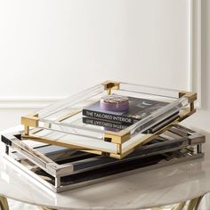 two glass trays with books on them sitting on top of a marble coffee table