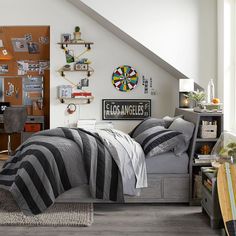 a bedroom with gray and black bedding, wooden shelves, and a desk in the corner