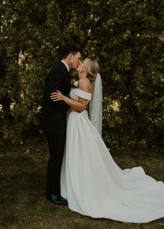 a bride and groom kissing in front of trees