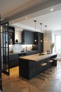 a kitchen with black cabinets and wooden flooring next to a dining room table filled with chairs