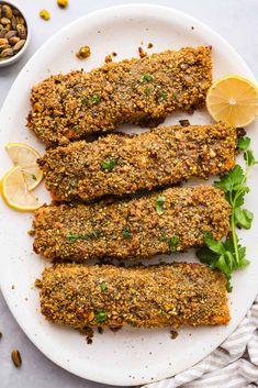 three pieces of breaded fish on a plate with lemon wedges and garnishes