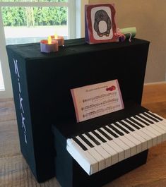 a piano made out of cardboard with a note on it and some candles next to it