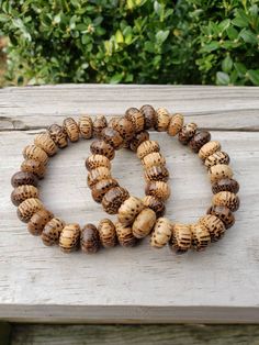 two bracelets made out of wood sitting on top of a wooden table next to bushes