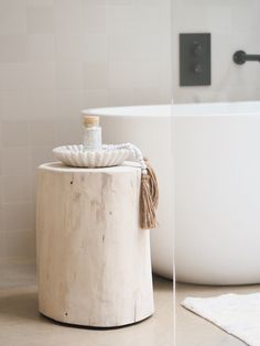 a white bath tub sitting next to a wooden stool with rope on the top and bottom