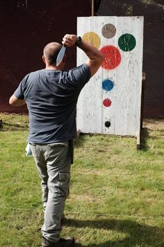 a man standing in front of a white board with circles painted on it and holding a knife up to his head