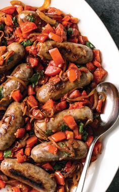 a white plate topped with sausages and carrots next to a silver serving spoon