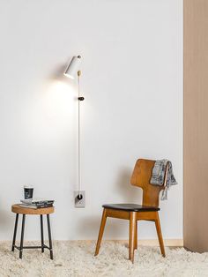 two chairs and a table in a room with white walls, one has a lamp on the wall