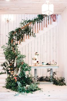 a table with flowers and greenery on it next to a stair case in a white room