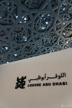 arabic writing on the side of a building with geometric designs above it and below that reads, louvre abu dhabi