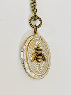 "This Bee locket featuring a brass oval vintage locket with lovely etching. I hand painted it in a shabby chic white. A tiny brass bee sits in the center. The locket hangs on a brass chain. You may choose your chain length at check out. The locket will arrive beautifully packaged and ready for gifting. Locket measures 1 and 3/8\" long and approximately 1 inch across." Vintage Jewelry With Oval Pendant Charms, Vintage Charm Oval Pendant Locket Necklace In Brass, Vintage Brass Locket Necklace With Oval Pendant, White Oval Pendant Locket Necklace, White Oval Pendant Necklace With Locket, Antique Oval White Necklace, Antique White Oval Necklace, White Oval Pendant Locket Jewelry, White Medallion Locket Necklace