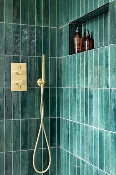 a green tiled shower with thermostaer and soap dispenser in it